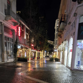 night view of a street in Athens. Shop lights are on and the cobblestone streets are wet